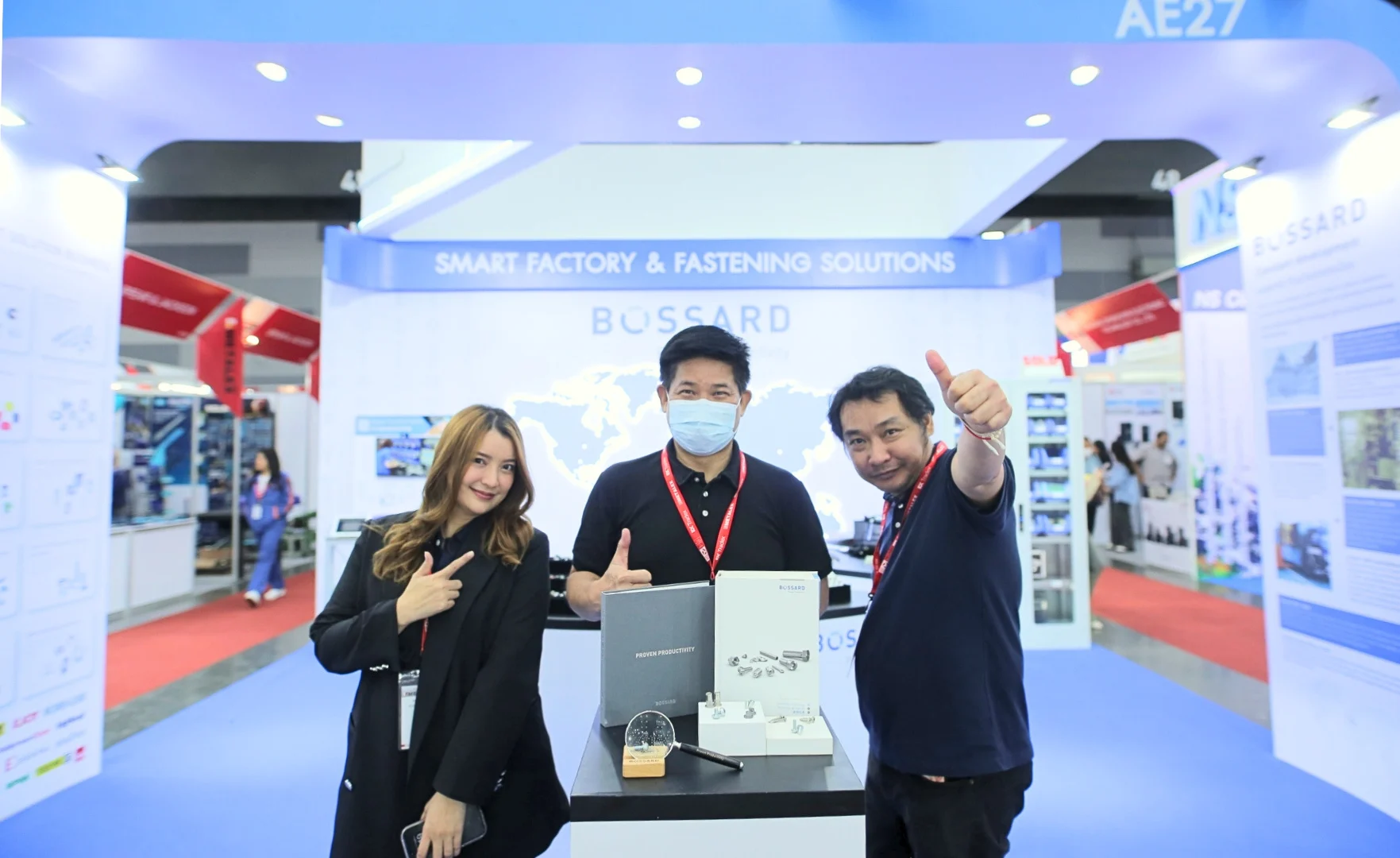 三名Bossard员工在展会的展台前，展台上标有“Smart Factory & Fastening Solutions”，展示了Bossard的品牌。